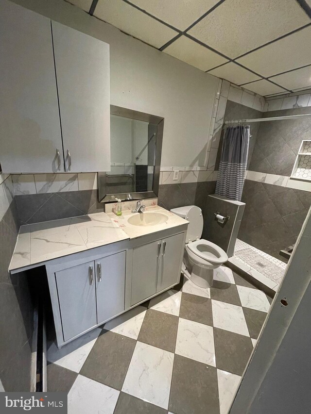 bathroom with curtained shower, toilet, a paneled ceiling, tile walls, and vanity