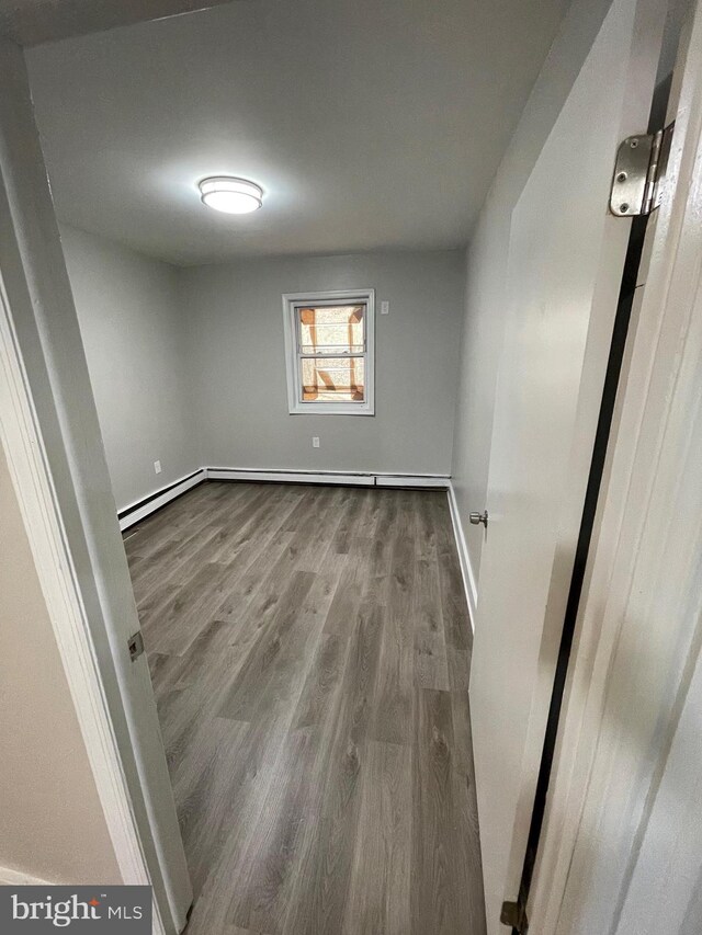 unfurnished room featuring a baseboard heating unit and wood-type flooring