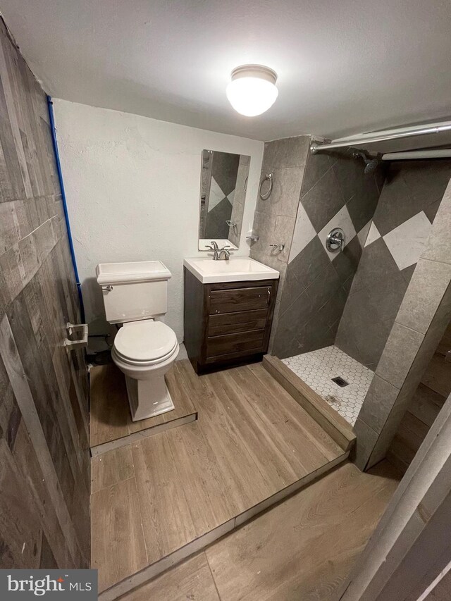 bathroom featuring a tile shower, wood-type flooring, toilet, tile walls, and vanity