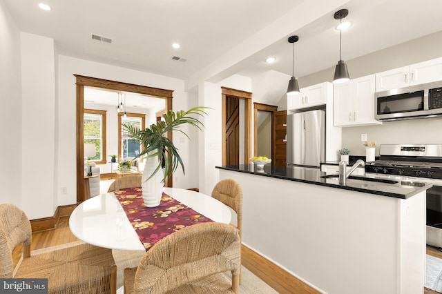 kitchen featuring stainless steel appliances, a center island, light hardwood / wood-style floors, white cabinetry, and hanging light fixtures