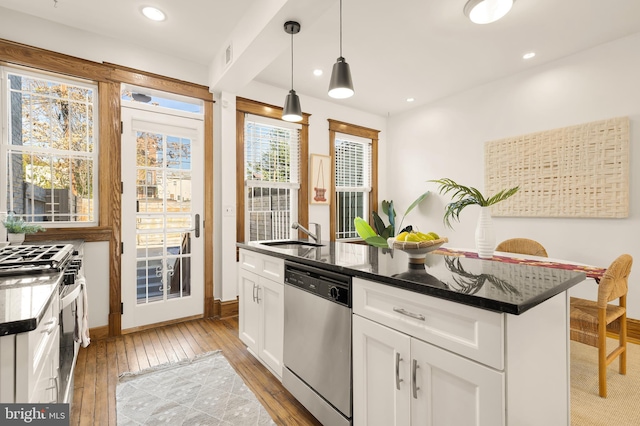 kitchen featuring stainless steel appliances, an island with sink, pendant lighting, light hardwood / wood-style floors, and white cabinets