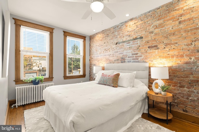 bedroom featuring radiator, ceiling fan, brick wall, and hardwood / wood-style flooring