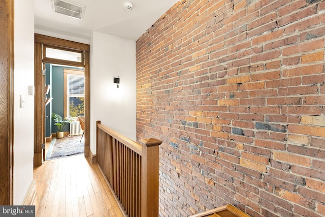 corridor with light hardwood / wood-style flooring and brick wall