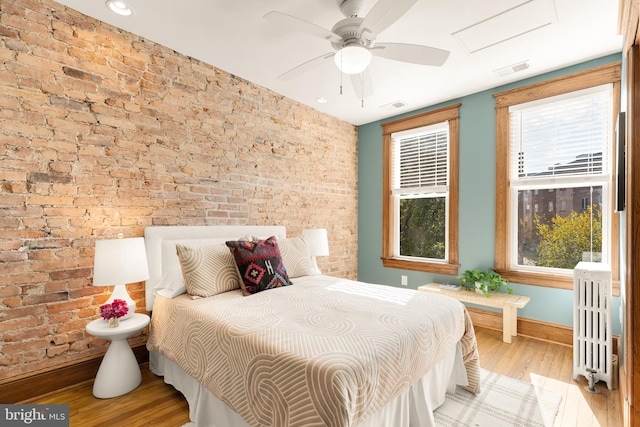 bedroom with ceiling fan, light hardwood / wood-style floors, radiator heating unit, and multiple windows