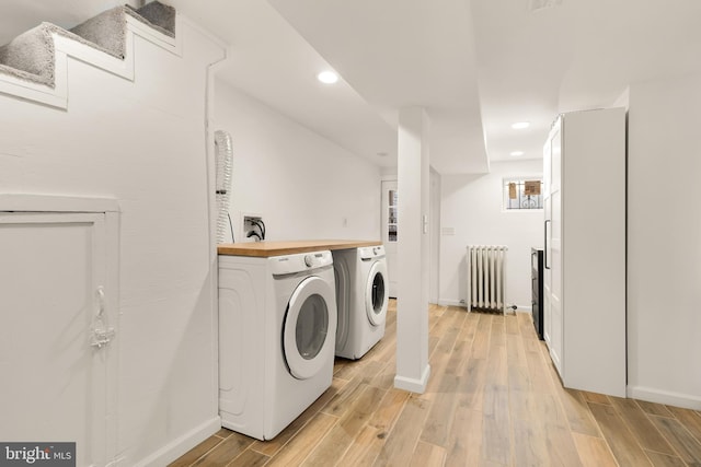 laundry area featuring washing machine and clothes dryer, radiator heating unit, and light hardwood / wood-style floors