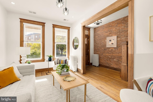 living area featuring radiator heating unit, light hardwood / wood-style flooring, and brick wall