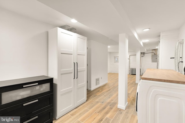 kitchen with wooden counters, light hardwood / wood-style flooring, white cabinets, radiator heating unit, and washer / clothes dryer