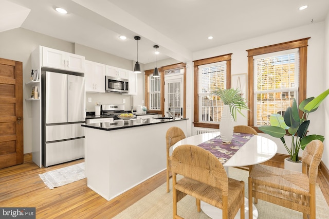 kitchen with light hardwood / wood-style flooring, white cabinets, hanging light fixtures, and appliances with stainless steel finishes