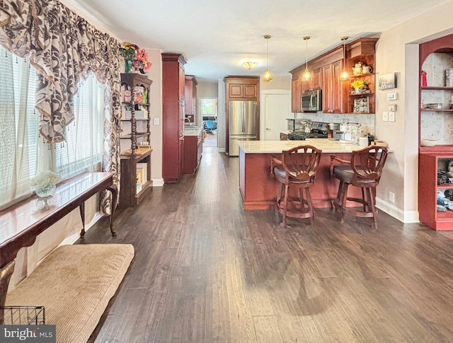 kitchen with decorative backsplash, hanging light fixtures, kitchen peninsula, stainless steel appliances, and dark hardwood / wood-style flooring