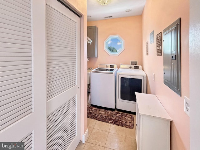 washroom featuring electric panel, light tile patterned flooring, washing machine and dryer, and cabinets