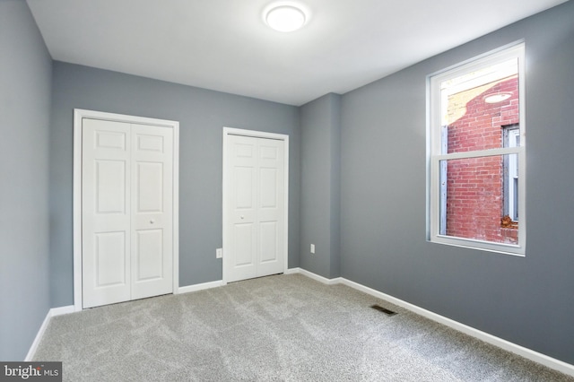 unfurnished bedroom featuring multiple closets and light colored carpet