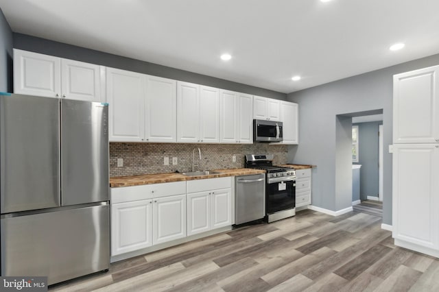 kitchen featuring white cabinets, decorative backsplash, appliances with stainless steel finishes, light hardwood / wood-style flooring, and sink