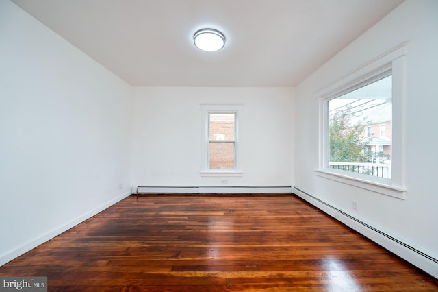 unfurnished room with a baseboard heating unit, a wealth of natural light, and dark hardwood / wood-style flooring