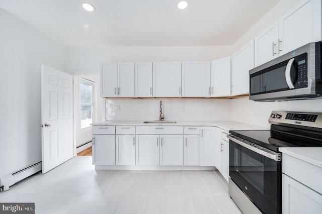 kitchen featuring a baseboard heating unit, sink, white cabinets, light tile patterned floors, and appliances with stainless steel finishes