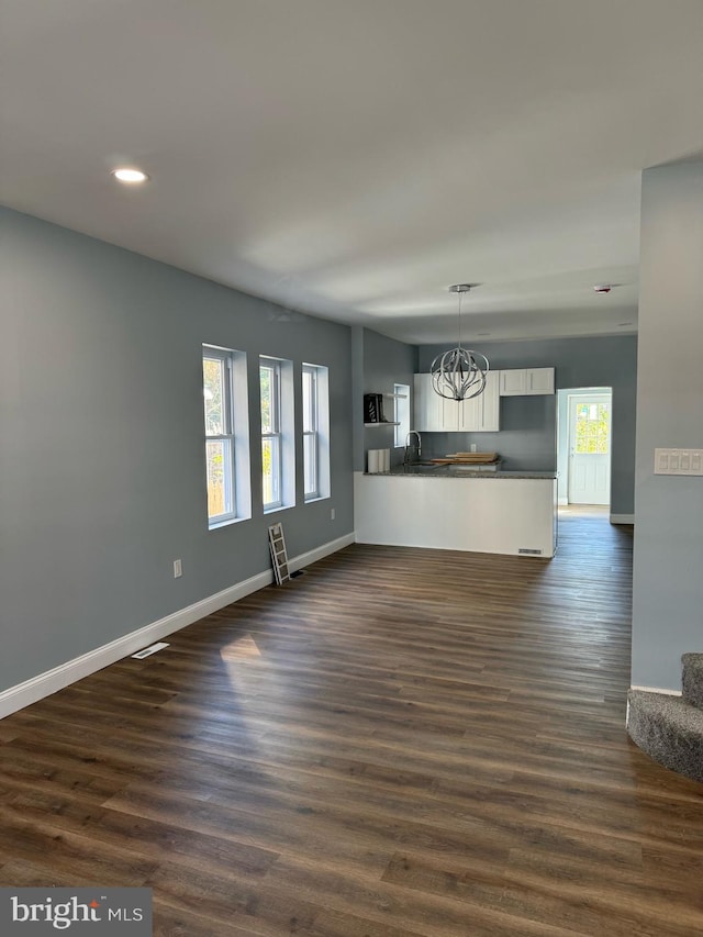 unfurnished living room featuring a chandelier, plenty of natural light, and dark hardwood / wood-style floors