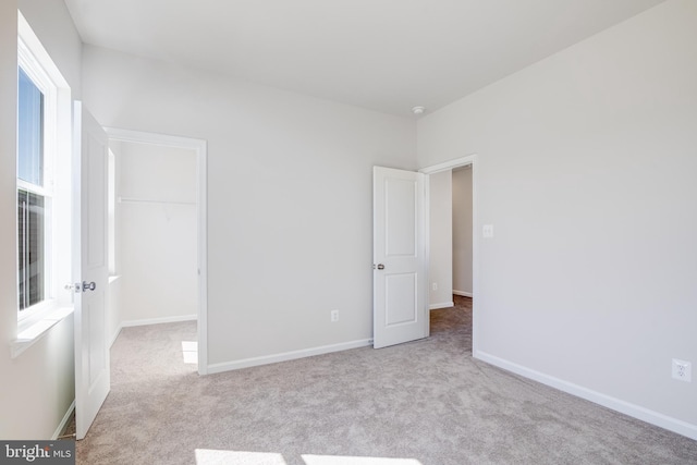 unfurnished bedroom with a walk in closet, a closet, and light colored carpet