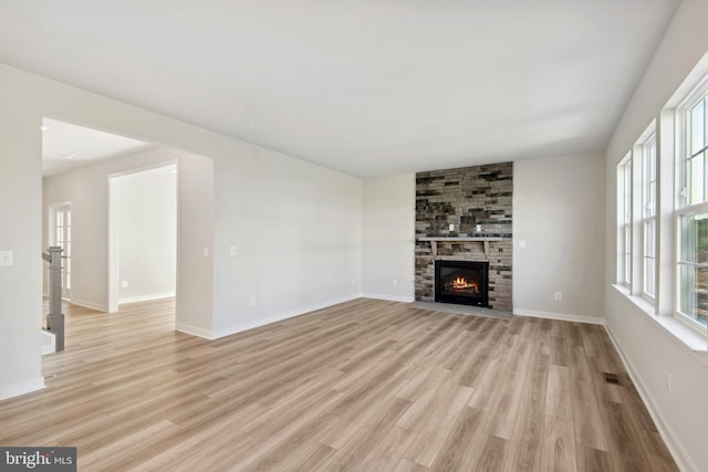 unfurnished living room featuring a stone fireplace, light wood-type flooring, and a wealth of natural light