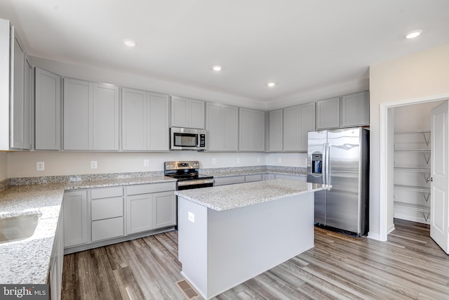 kitchen with gray cabinetry, a center island, stainless steel appliances, light stone counters, and light hardwood / wood-style flooring