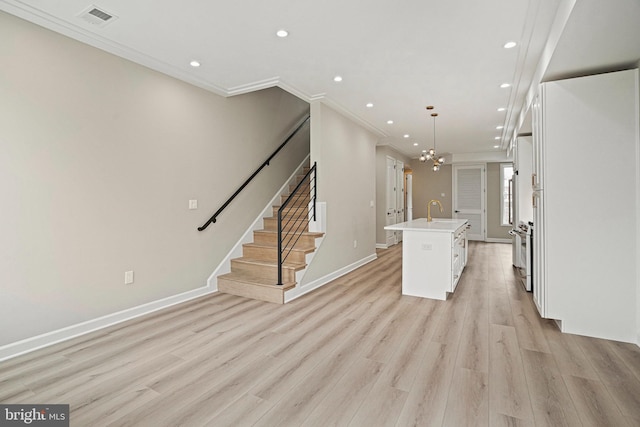 kitchen with light wood-type flooring, decorative light fixtures, a notable chandelier, white cabinets, and an island with sink