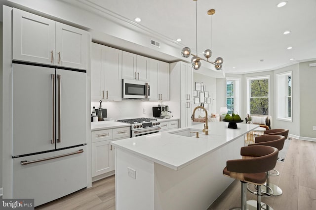 kitchen featuring high end appliances, sink, an island with sink, a kitchen bar, and white cabinetry