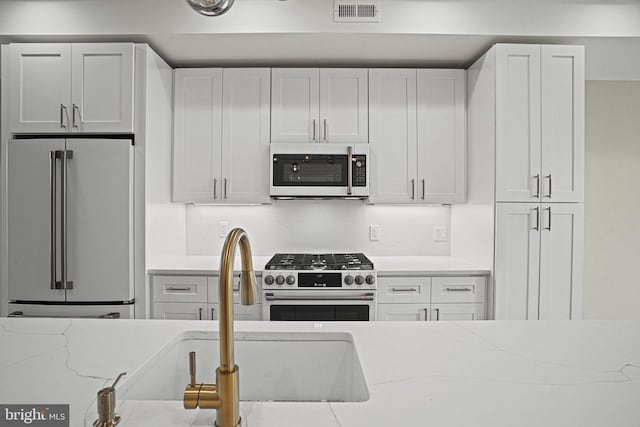 kitchen with white cabinets, premium appliances, light stone counters, and decorative backsplash