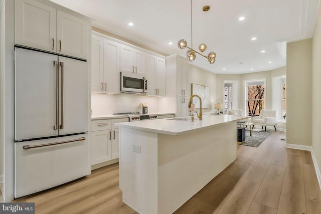 kitchen with a center island with sink, hanging light fixtures, light hardwood / wood-style flooring, white cabinetry, and high end white refrigerator