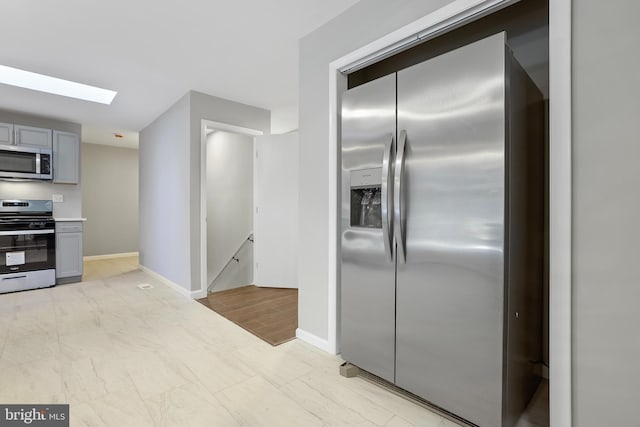 kitchen featuring stainless steel appliances, a skylight, light wood-type flooring, and gray cabinets