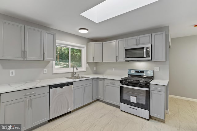 kitchen with gray cabinets, stainless steel appliances, sink, and a skylight