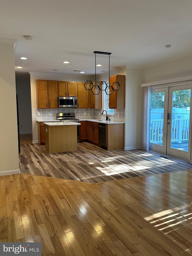 kitchen with a kitchen island, stainless steel appliances, wood-type flooring, ornamental molding, and pendant lighting