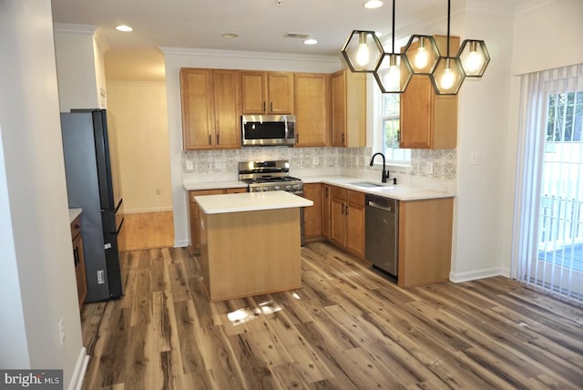 kitchen featuring wood-type flooring, appliances with stainless steel finishes, sink, a kitchen island, and hanging light fixtures