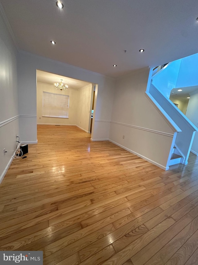 unfurnished living room with a notable chandelier, ornamental molding, and light wood-type flooring