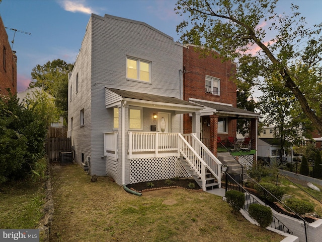 view of front facade with covered porch, central AC, and a lawn