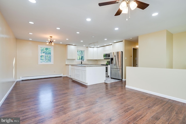 kitchen with dark wood-type flooring, white cabinets, decorative backsplash, baseboard heating, and appliances with stainless steel finishes