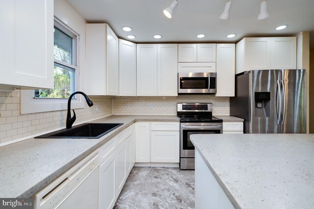 kitchen featuring stainless steel appliances, light stone counters, white cabinetry, and sink