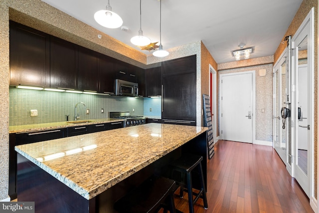 kitchen with tasteful backsplash, light stone countertops, stainless steel microwave, a sink, and range with gas stovetop