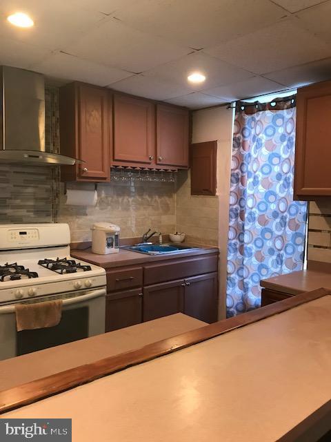 kitchen with wall chimney exhaust hood, tasteful backsplash, a sink, and white range with gas stovetop
