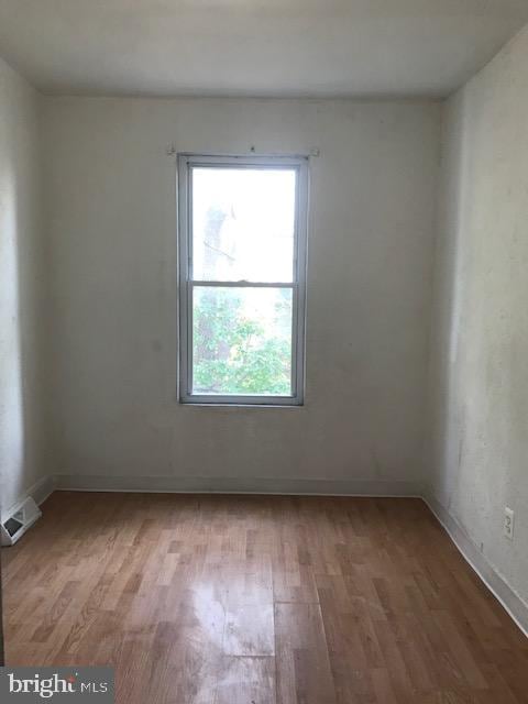 spare room featuring wood finished floors, visible vents, and baseboards