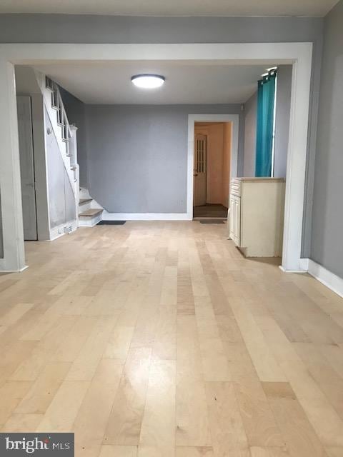 empty room featuring baseboards, light wood-style floors, and stairway