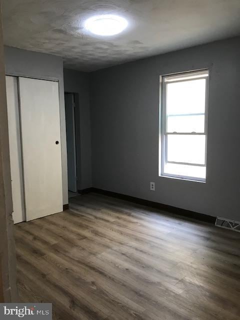 unfurnished bedroom with baseboards, wood finished floors, visible vents, and a closet