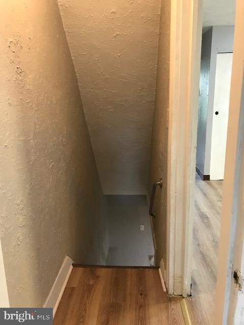 stairway featuring lofted ceiling, a textured wall, and wood finished floors