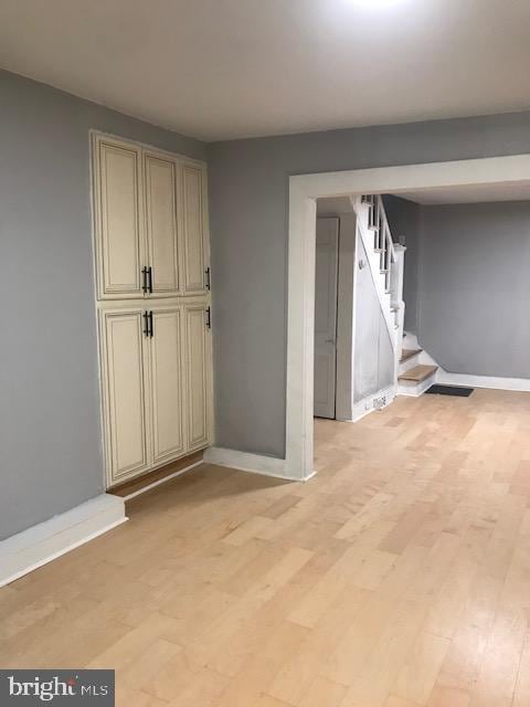 spare room featuring baseboards, light wood-style floors, and stairs
