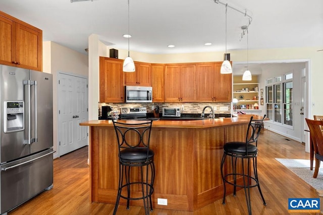 kitchen featuring pendant lighting, an island with sink, stainless steel appliances, and light wood-type flooring