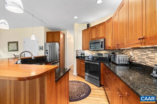 kitchen featuring sink, backsplash, light hardwood / wood-style floors, stainless steel appliances, and pendant lighting