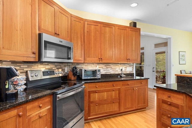 kitchen featuring dark stone countertops, tasteful backsplash, appliances with stainless steel finishes, and light wood-type flooring