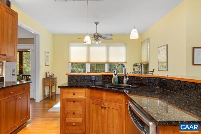 kitchen with light hardwood / wood-style floors, dark stone countertops, stainless steel dishwasher, and plenty of natural light