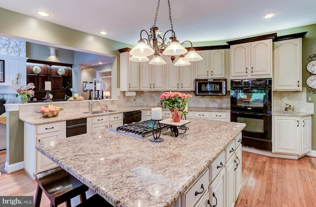 kitchen with black appliances, light wood-type flooring, a kitchen island, kitchen peninsula, and hanging light fixtures