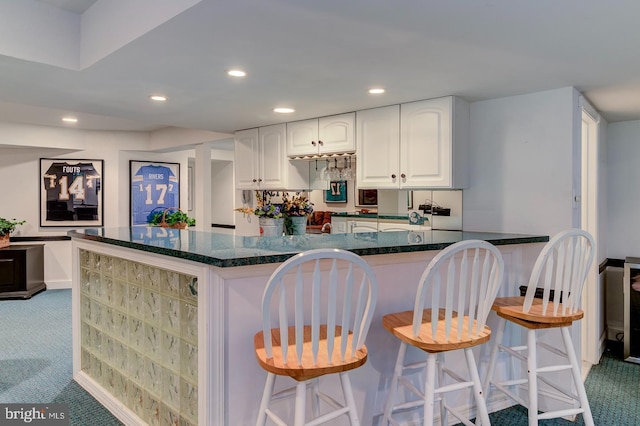 kitchen featuring carpet, white cabinetry, a kitchen breakfast bar, and dark stone countertops