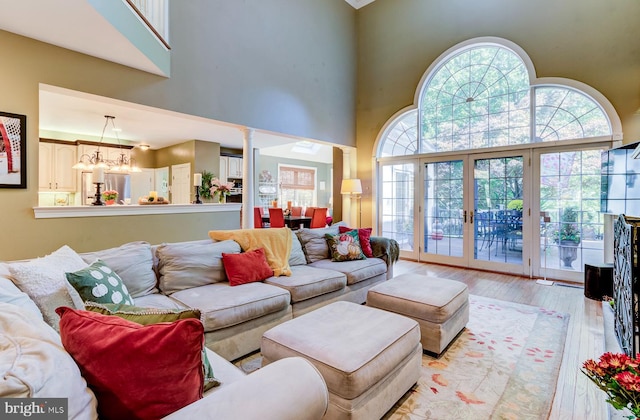 living room with a towering ceiling, a chandelier, ornate columns, and light wood-type flooring