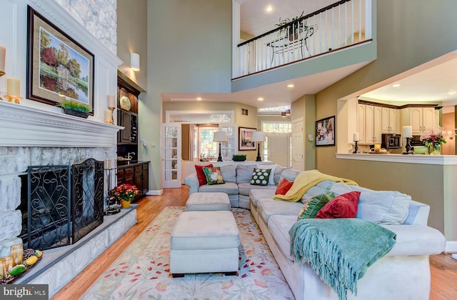 living room with a stone fireplace, a high ceiling, and light wood-type flooring