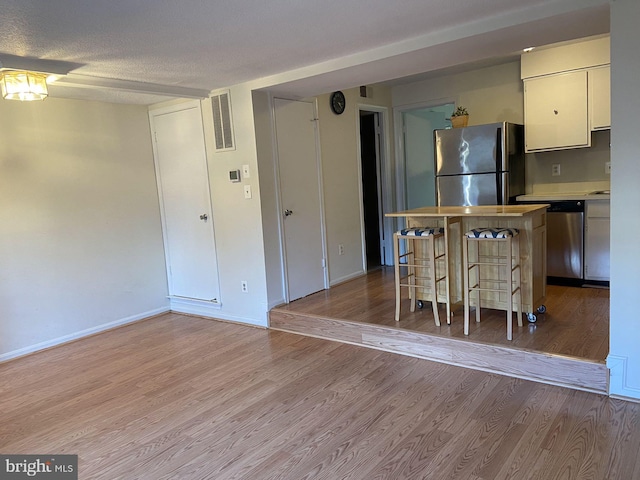 kitchen featuring a kitchen island, a textured ceiling, a kitchen breakfast bar, stainless steel appliances, and light hardwood / wood-style flooring